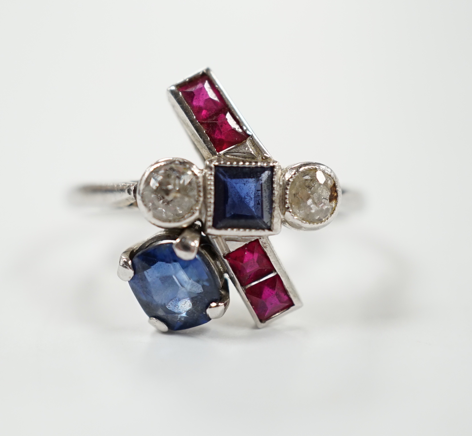 An unusual 1920's/1930's platinum, ruby, sapphire and diamond cluster set dress ring, of free form, the stones in a millegrain, claw or collet settings, size I, gross weight 3.7 grams.
